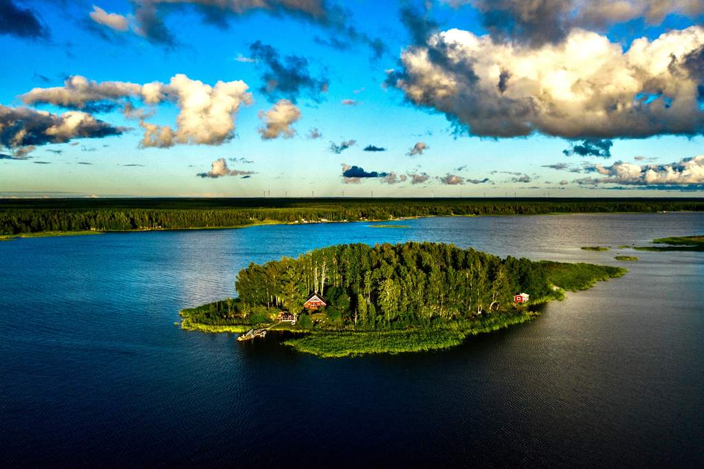 Majorsgrund from the air: a wooded island with red log houses in a calm, dark blue sea
